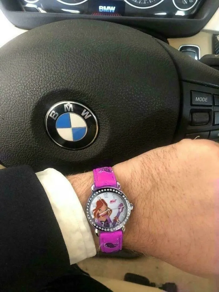 Man wearing a pink cartoon watch while holding a BMW steering wheel, creating a weird and confusing visual contrast.