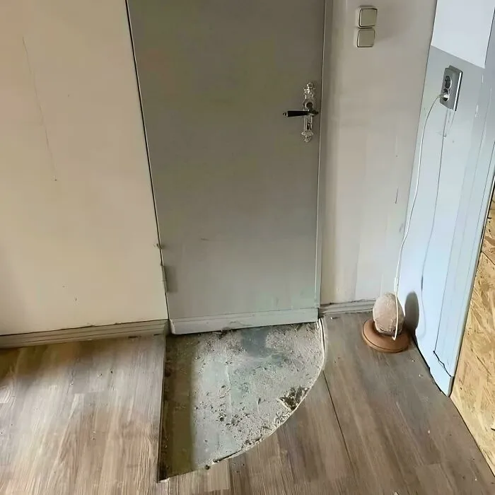 Partially removed wooden floor revealing concrete underneath in a confusing and weird interior room scene.