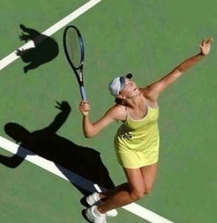 Tennis player serving on court with shadow creating a weird and confusing visual effect.