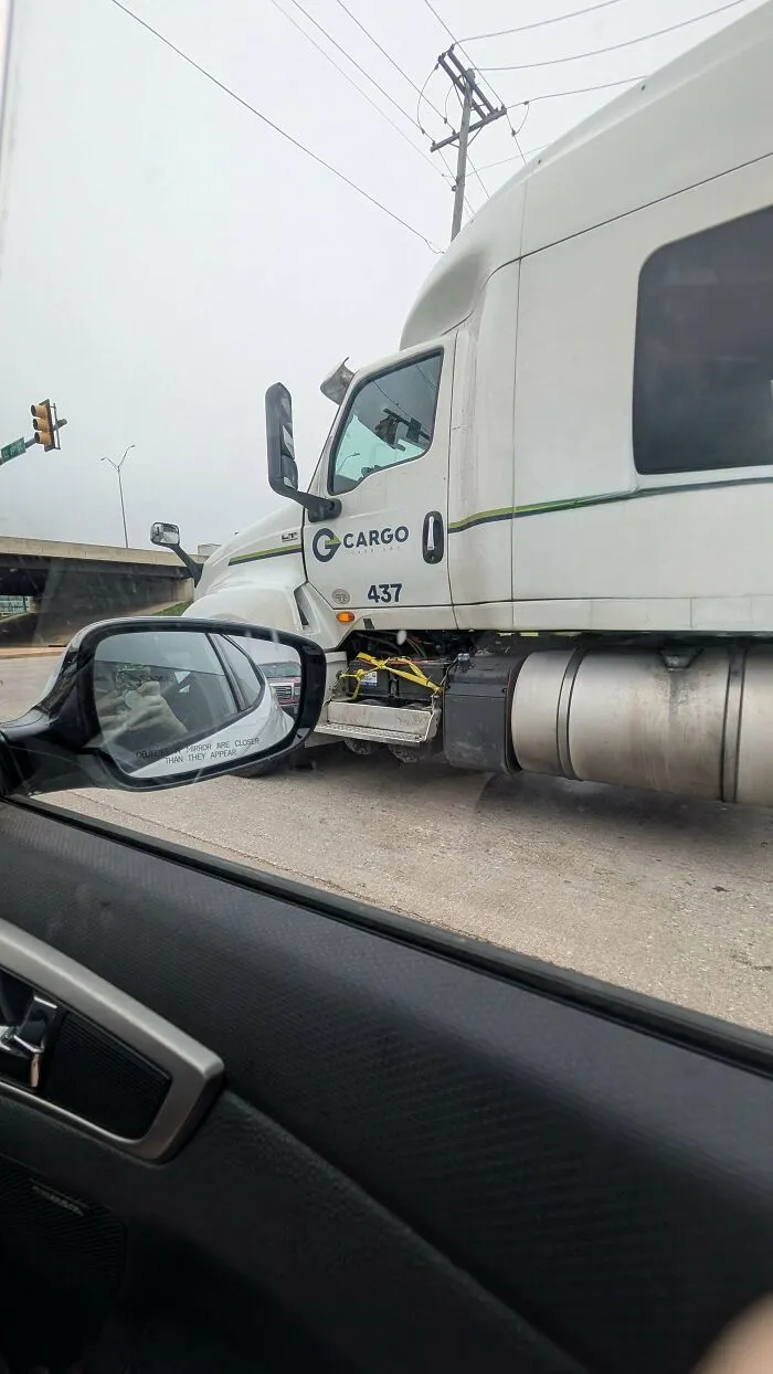 View from car window showing a truck with a hilariously dumb but technically works tie-down solution at the side step.