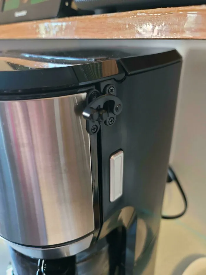 Coffee maker with a latch installed to keep the lid closed, a hilariously dumb but technically works solution to the problem.