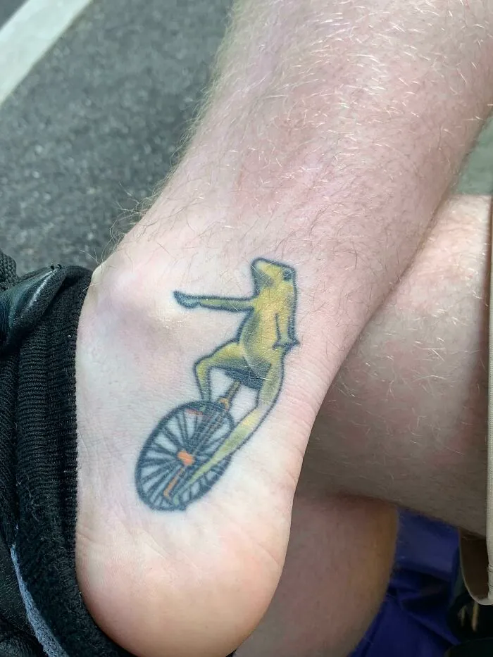 Weird unicycling frog tattoo on ankle showcasing craftsmanship