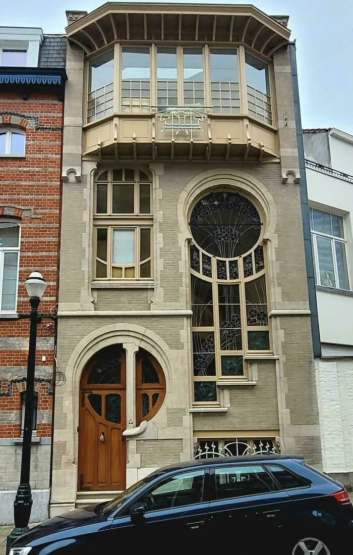 Unique and beautiful architecture of a building facade with an arched wooden door, large decorative windows, and a car in front.