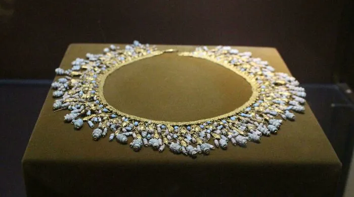 Ancient artefact necklace with detailed blue and gold beads displayed on a dark velvet surface for historical perspective.