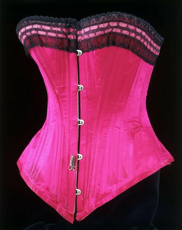 Bright pink vintage corset with black lace trim, a historical garment showcasing 19th century fashion and intricate detailing.