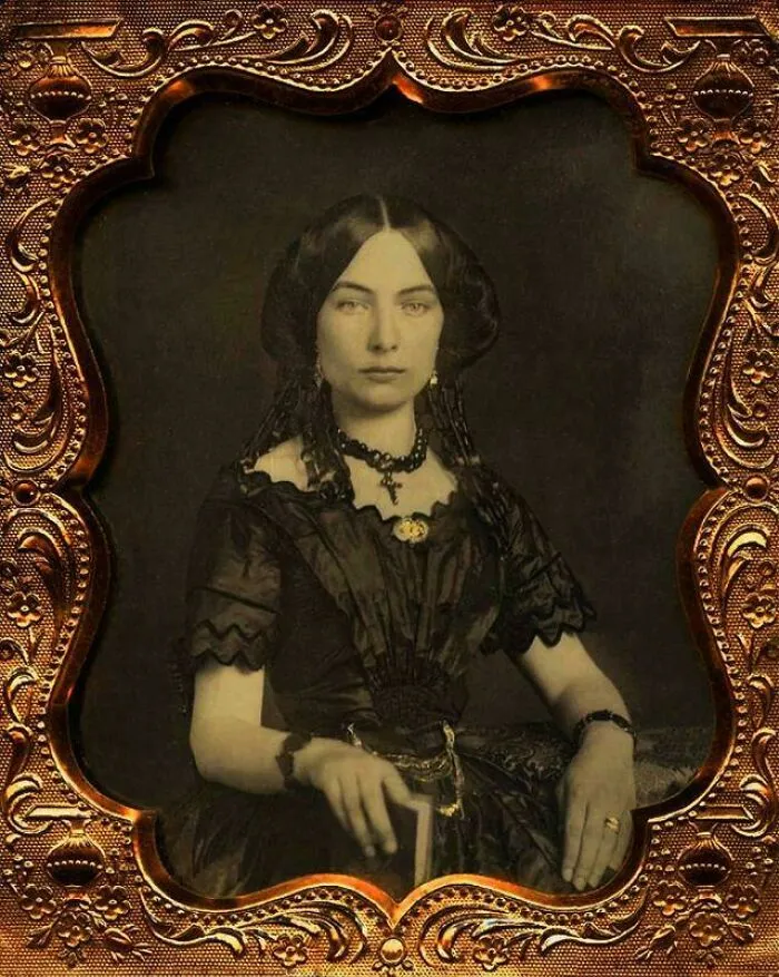 Victorian-era woman in an ornate historical garment, seated with jewelry, holding a book in a decorative vintage frame.