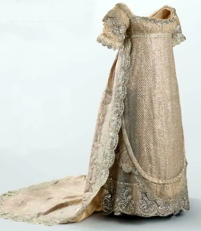 Embroidered historical garment with lace detailing and a long train, showcasing vintage textile craftsmanship and style.