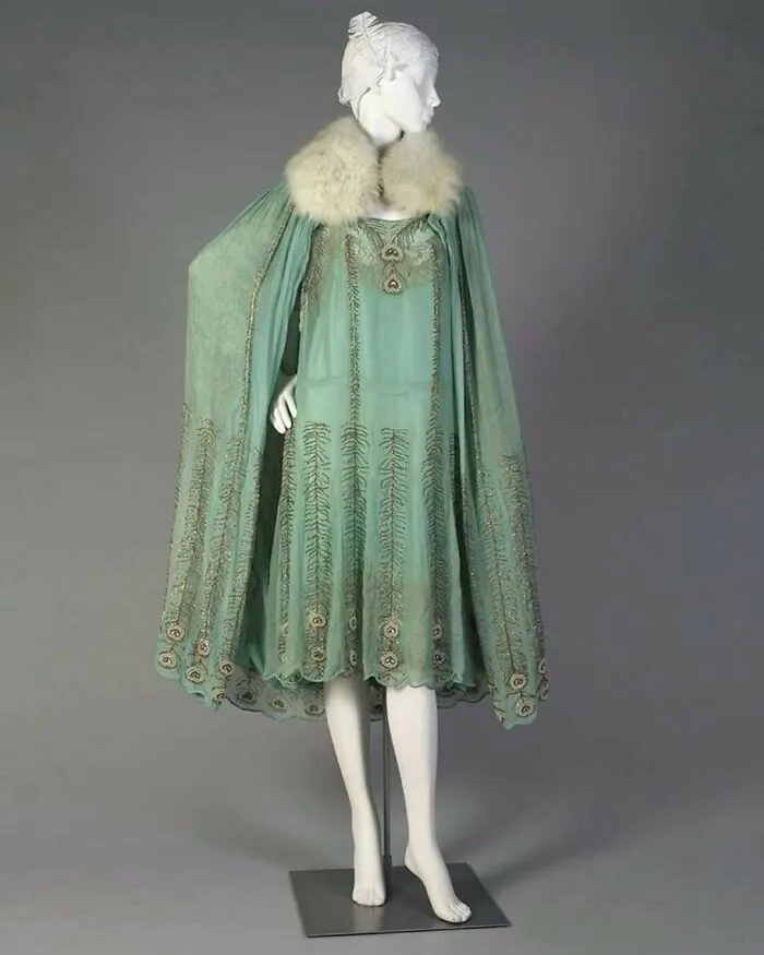 Mannequin dressed in a vintage historical garment featuring a green embroidered dress with a fur collar cape.