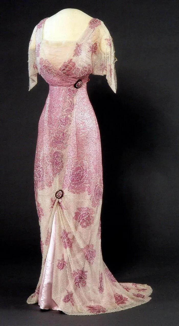 Early 20th century historical garment, elegant pink beaded dress with floral patterns and decorative brooches on display.