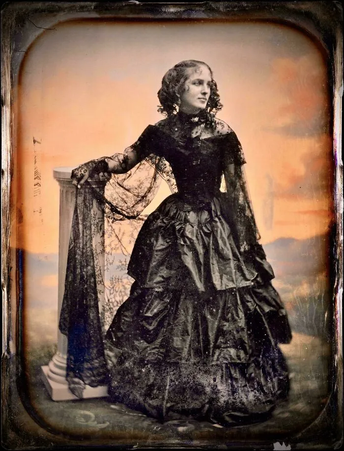 Victorian woman wearing an elaborate historical garment with lace details and a voluminous skirt posing indoors.