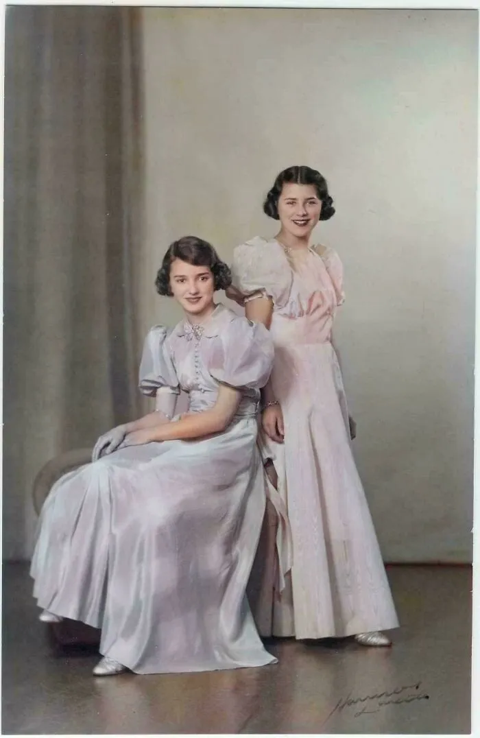 Two women in vintage dresses with puff sleeves posing for a formal studio photo from decades ago, classic portrait style.
