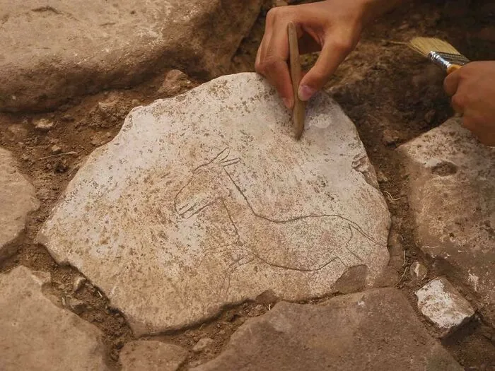 Ancient artefact with animal engraving being uncovered by archaeologists using tools in an excavation site.