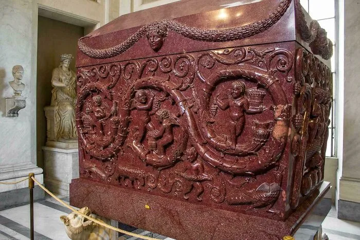 Intricately carved ancient red marble sarcophagus displayed indoors as a fascinating artefact of human history.