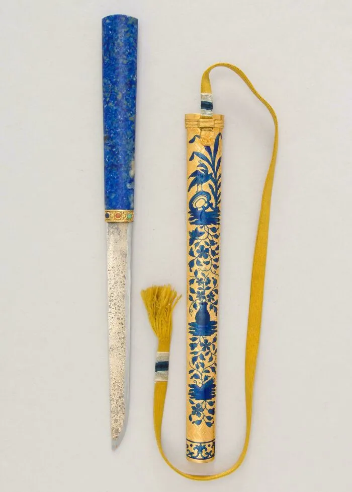 Ancient decorated dagger with blue stone handle and ornate gold sheath featuring intricate blue floral patterns.