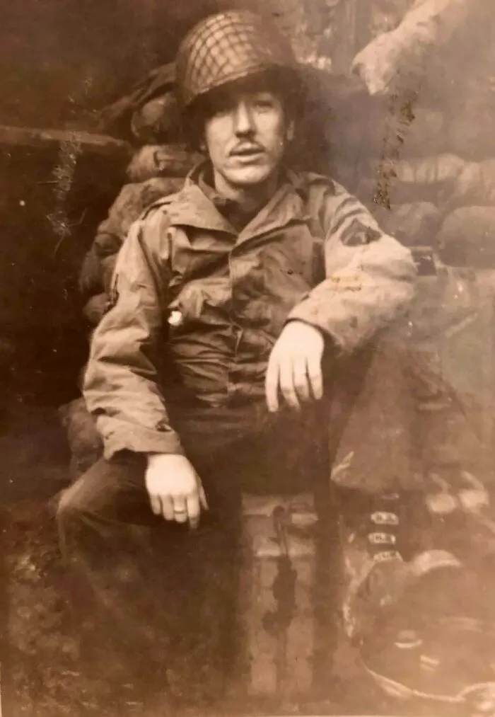 Black and white historical photo of a soldier in vintage military uniform sitting in a trench during wartime.