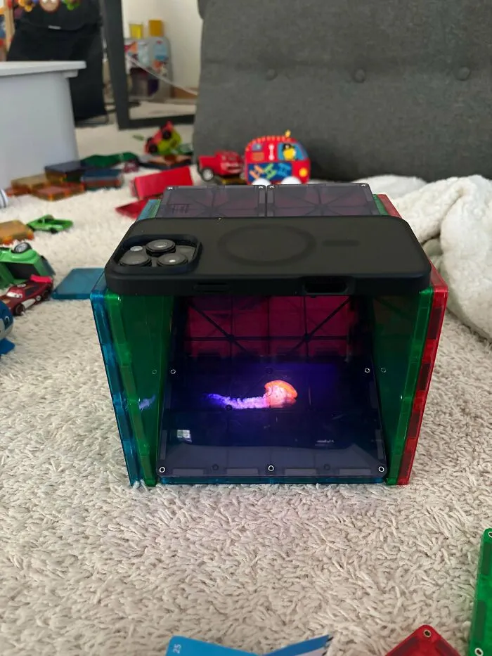 A phone placed on colorful magnetic blocks displaying a glowing jellyfish, illustrating a wholesome, funny, and goofy dad activity.