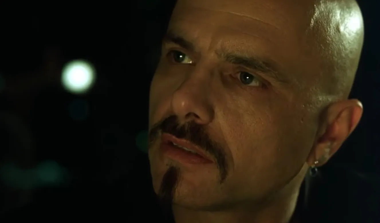 Cypher from The Matrix in a close-up shot with intense expression in a dark background scene.
