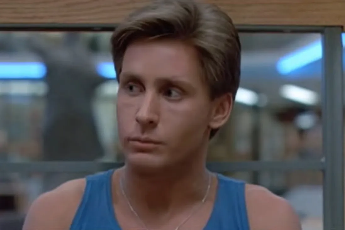 Andrew from The Breakfast Club wearing a blue tank top, looking to the side in a school library setting.