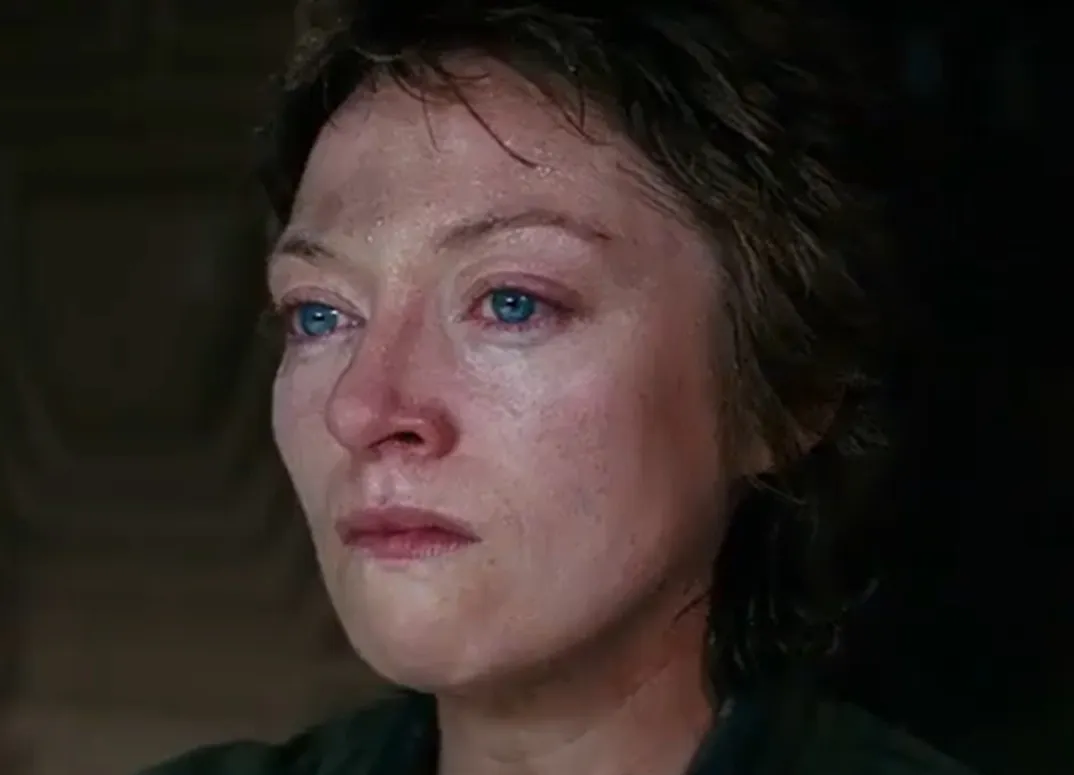 Close-up of Lambert from Alien, showing a pensive expression with blue eyes and short hair in dim lighting.