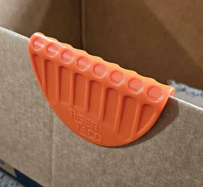 Herramienta Tiger Taco naranja sujetando una caja de cartón. Genial e inusual para simplificar tu vida.