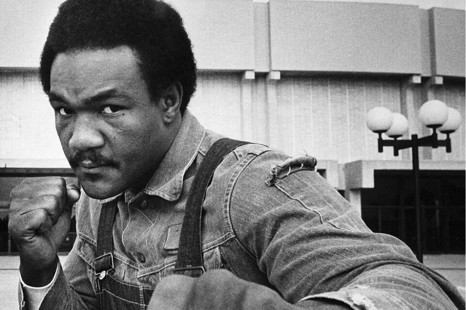 George Foreman posing with fists raised outdoors in a black and white photo related to boxing history.