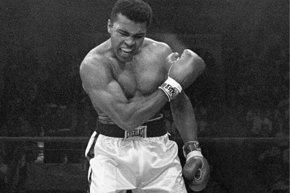 Muhammad Ali celebrating a boxing victory wearing Everlast gloves and trunks during a famous 1974 match.