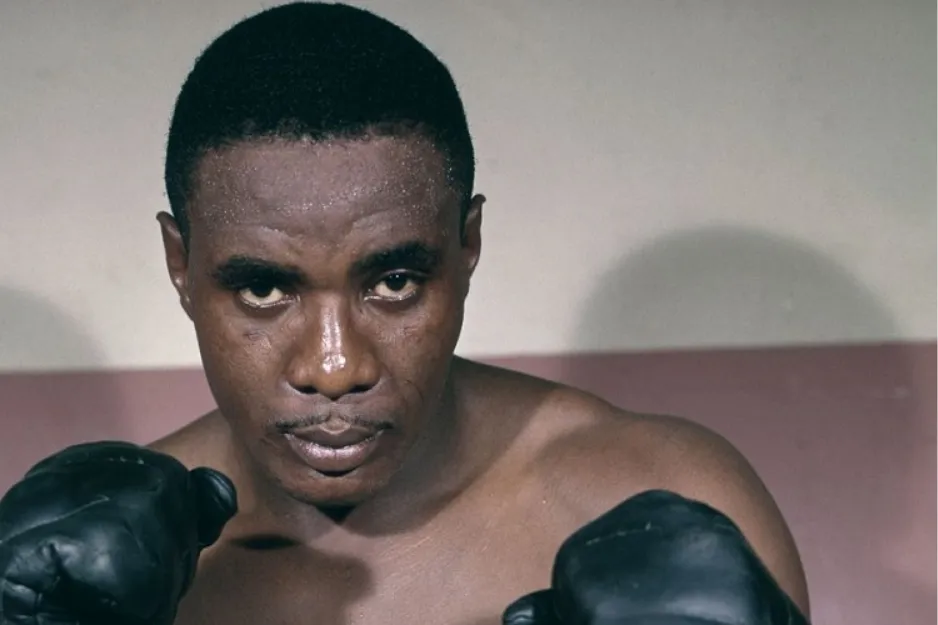 Boxer Sonny Liston posing with boxing gloves, preparing for a famous 1974 boxing match known as Rumble in the Jungle.