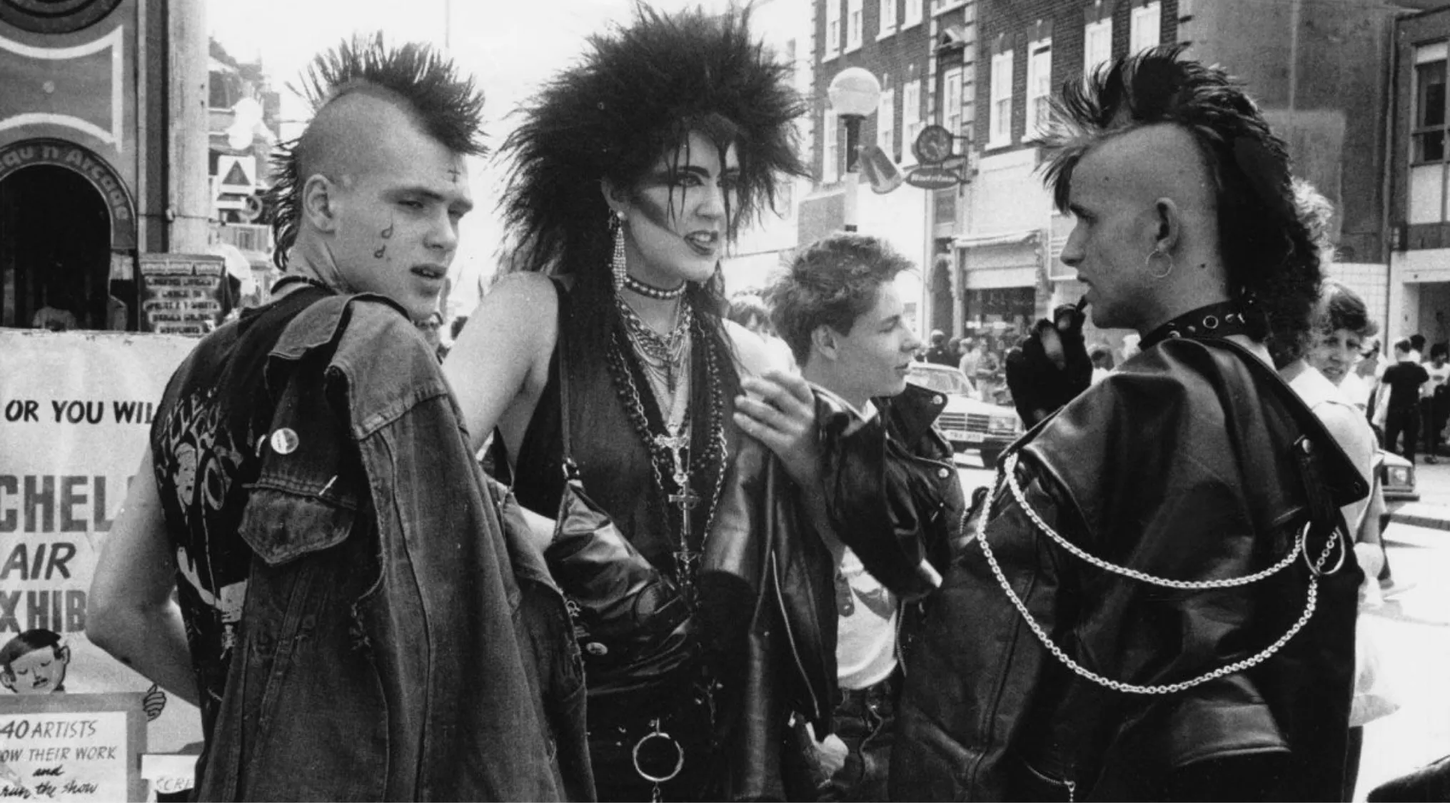 Group of young people dressed in punk fashion with mohawks, leather jackets, and bold hairstyles in a 1970s street setting.