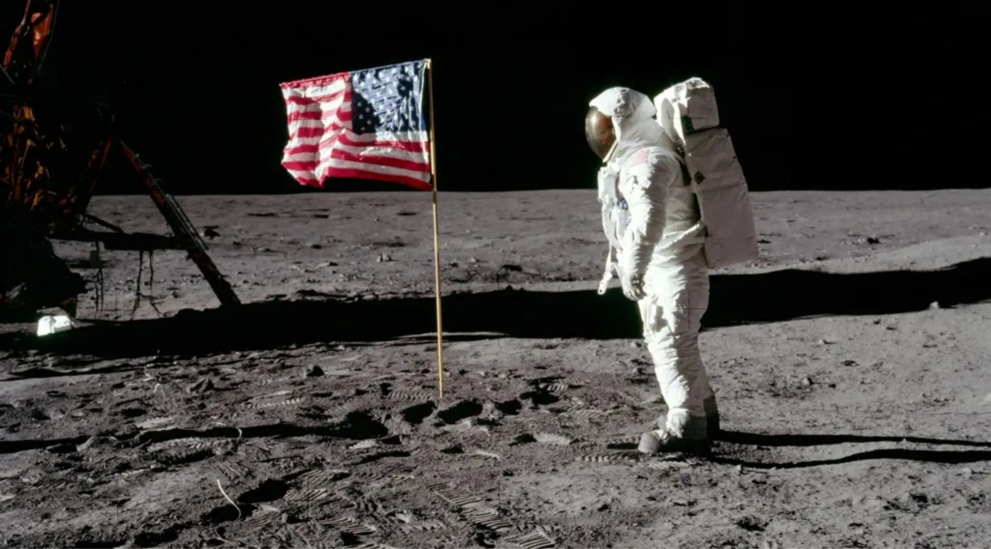Astronaut in spacesuit standing on the Moon near American flag during NASA moon landing mission.