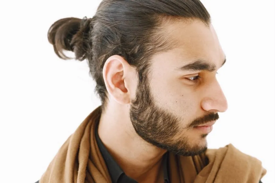 Side profile of a man with a man bun hairstyle, beard, and brown scarf, showcasing a popular 1970s men's look.