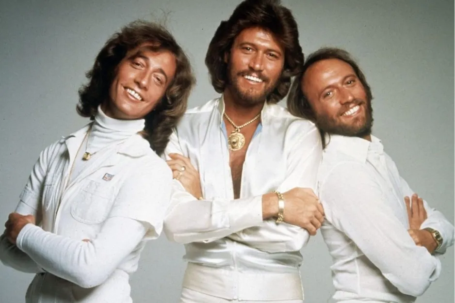 The Bee Gees band members posing together with arms crossed, wearing white outfits in a studio setting