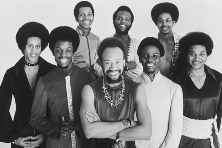 Seven members of Earth Wind and Fire smiling in vintage attire, posing for a black and white group portrait.