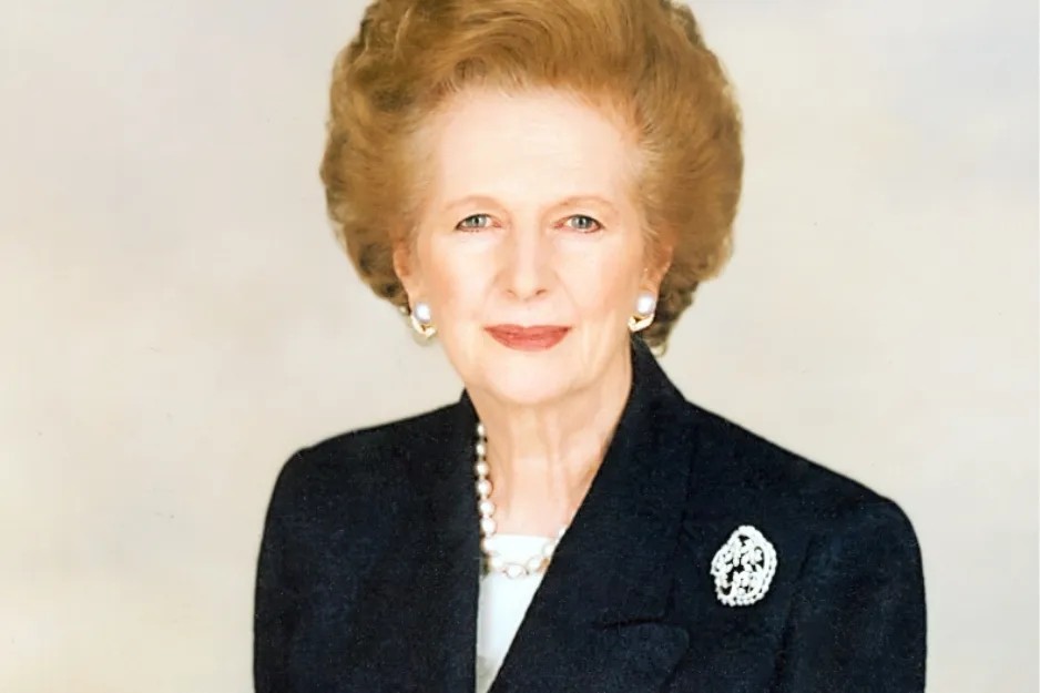 Portrait of an elderly woman with pearl earrings and necklace, wearing a dark blazer with a brooch.