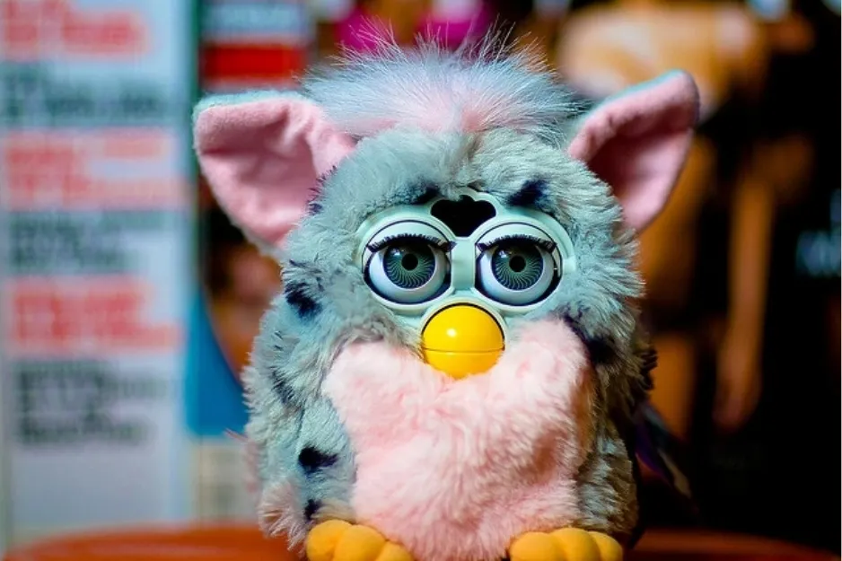 Close-up of a Furby toy with blue fur and yellow beak, a popular interactive toy introduced in the 1990s.