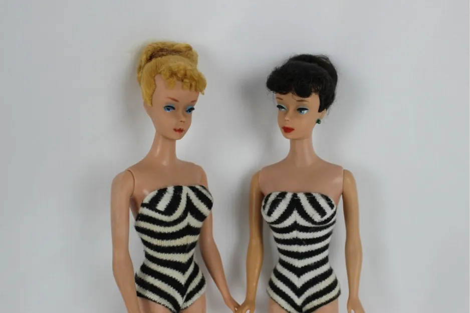 Two vintage Barbie dolls wearing black and white striped swimsuits against a plain white background.