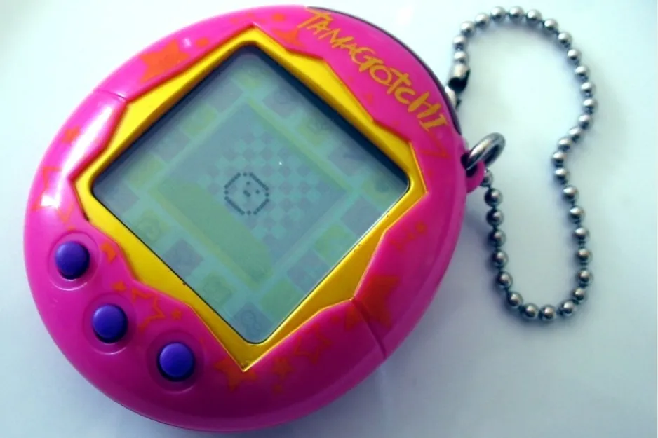 Pink and yellow Tamagotchi digital toy with a screen, three purple buttons, and a metal ball chain attached.