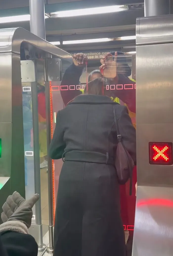 Person trapped in subway turnstile gate with red X signal in a weird moment on the NYC subway platform.