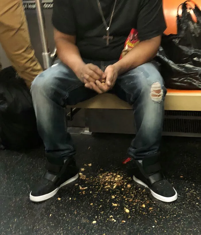 Man sitting on NYC subway seat with food crumbs scattered on floor beneath, capturing a weird subway moment.