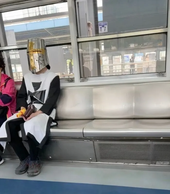 Person wearing a medieval knight helmet and outfit sitting on a NYC subway bench during a weird moment