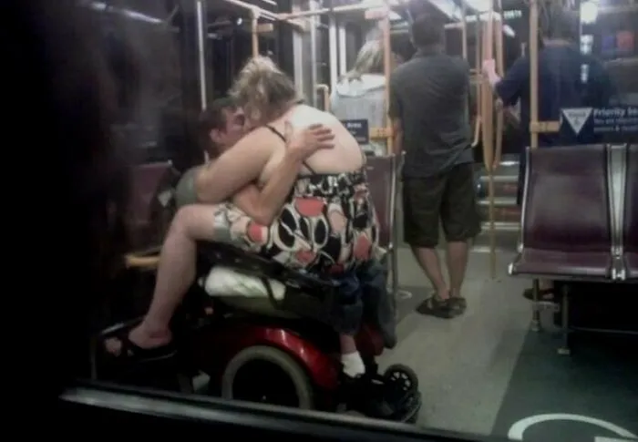 Couple embracing on a wheelchair inside a crowded NYC subway, capturing a weird subway moment off the rails.