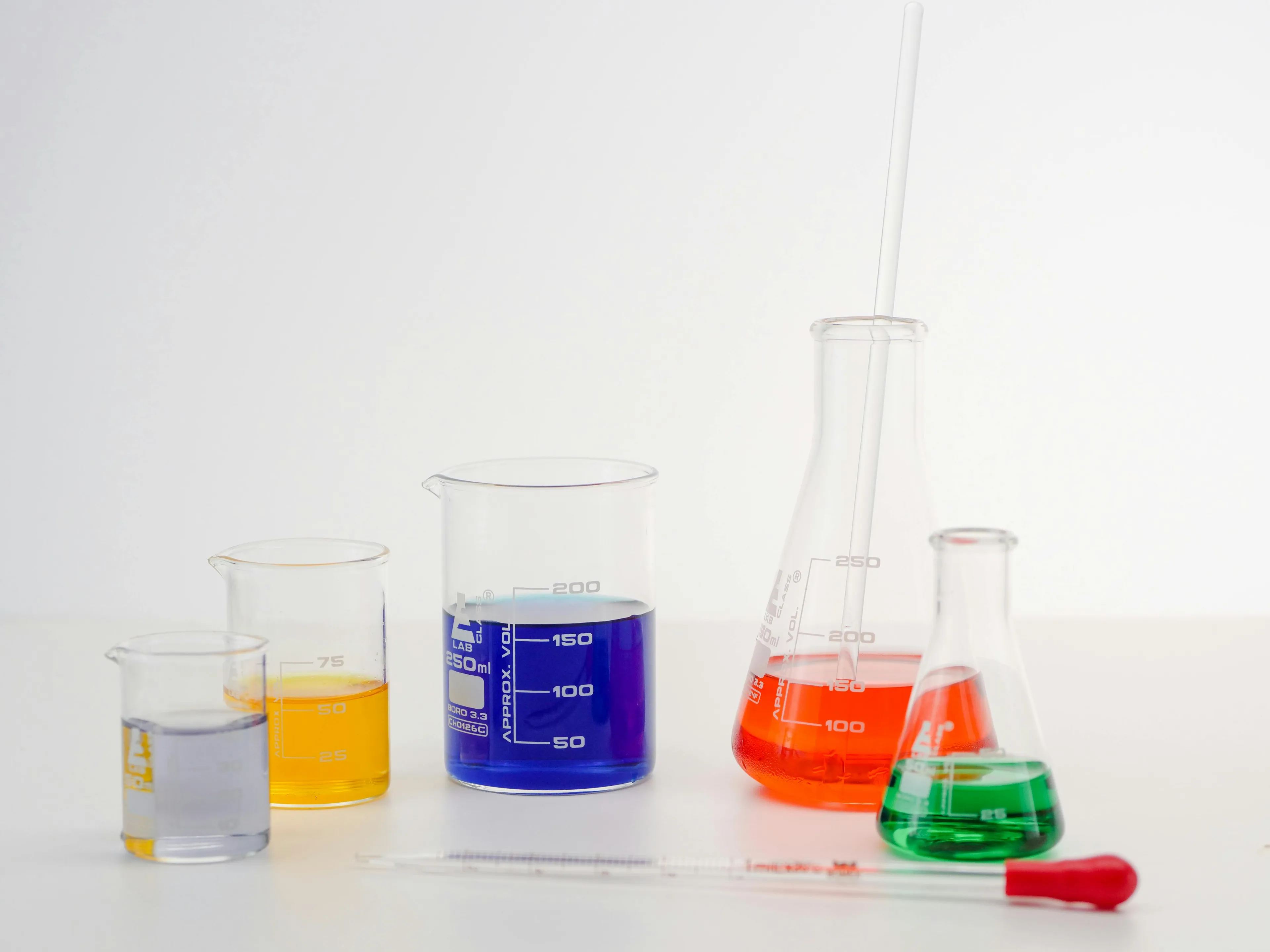 Lab glassware containing colored liquids used in GCSE combined science quiz about the pH of a neutral solution.