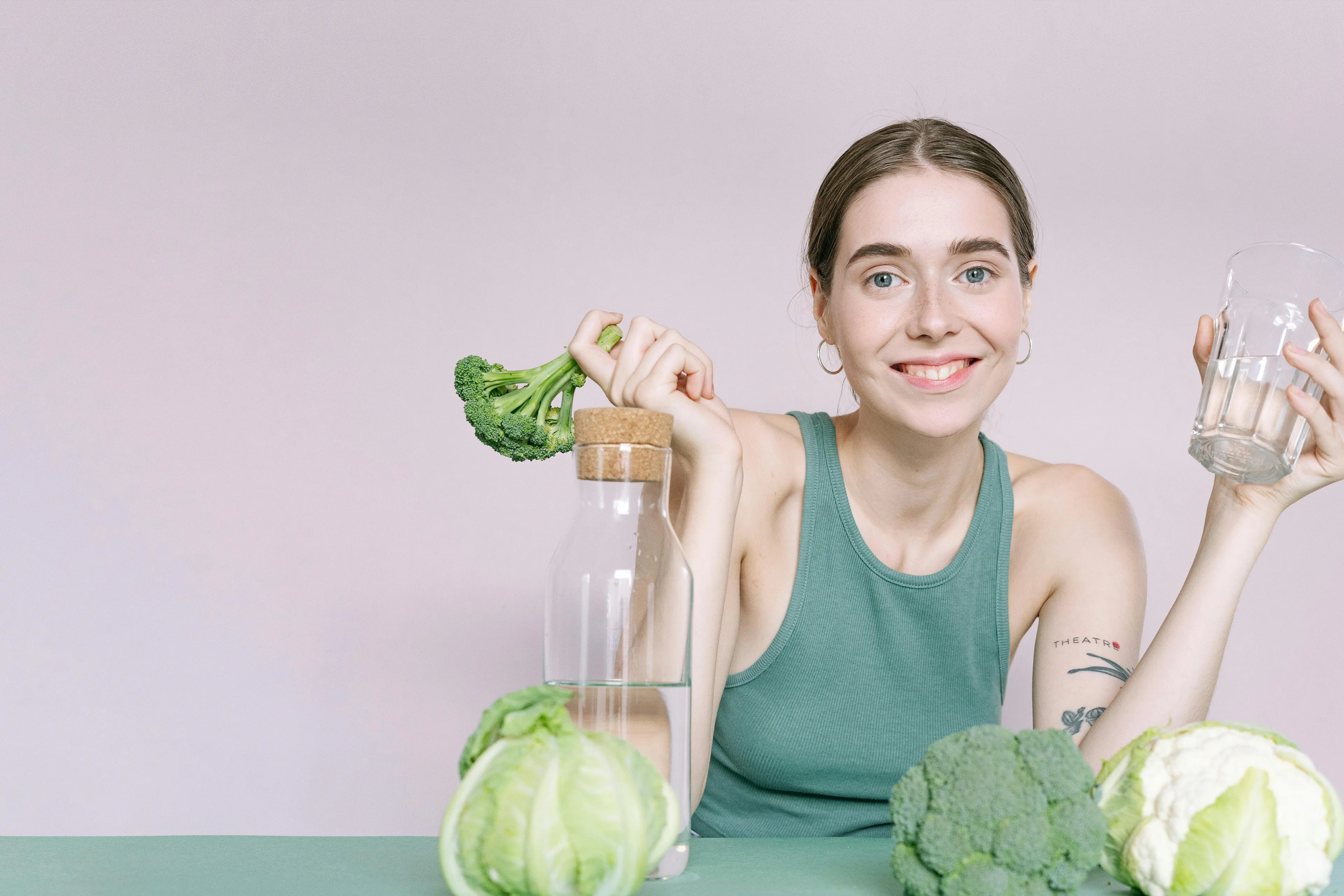 Young woman in green top holding broccoli and water glass, surrounded by vegetables, focusing on nutrient for growth and repair.