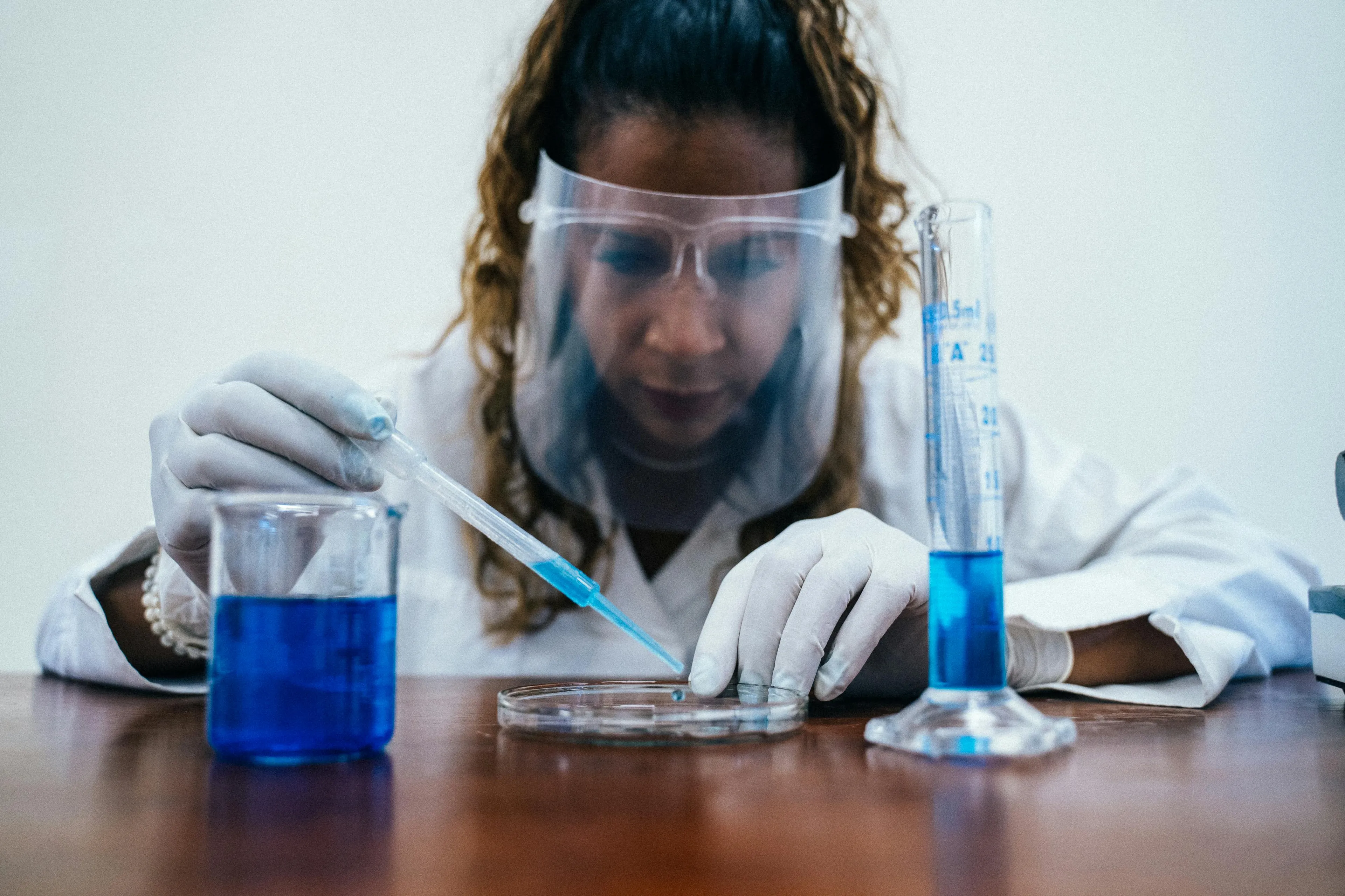 Scientist in protective gear using a pipette with blue liquid, demonstrating changes affecting chemical reaction speed.