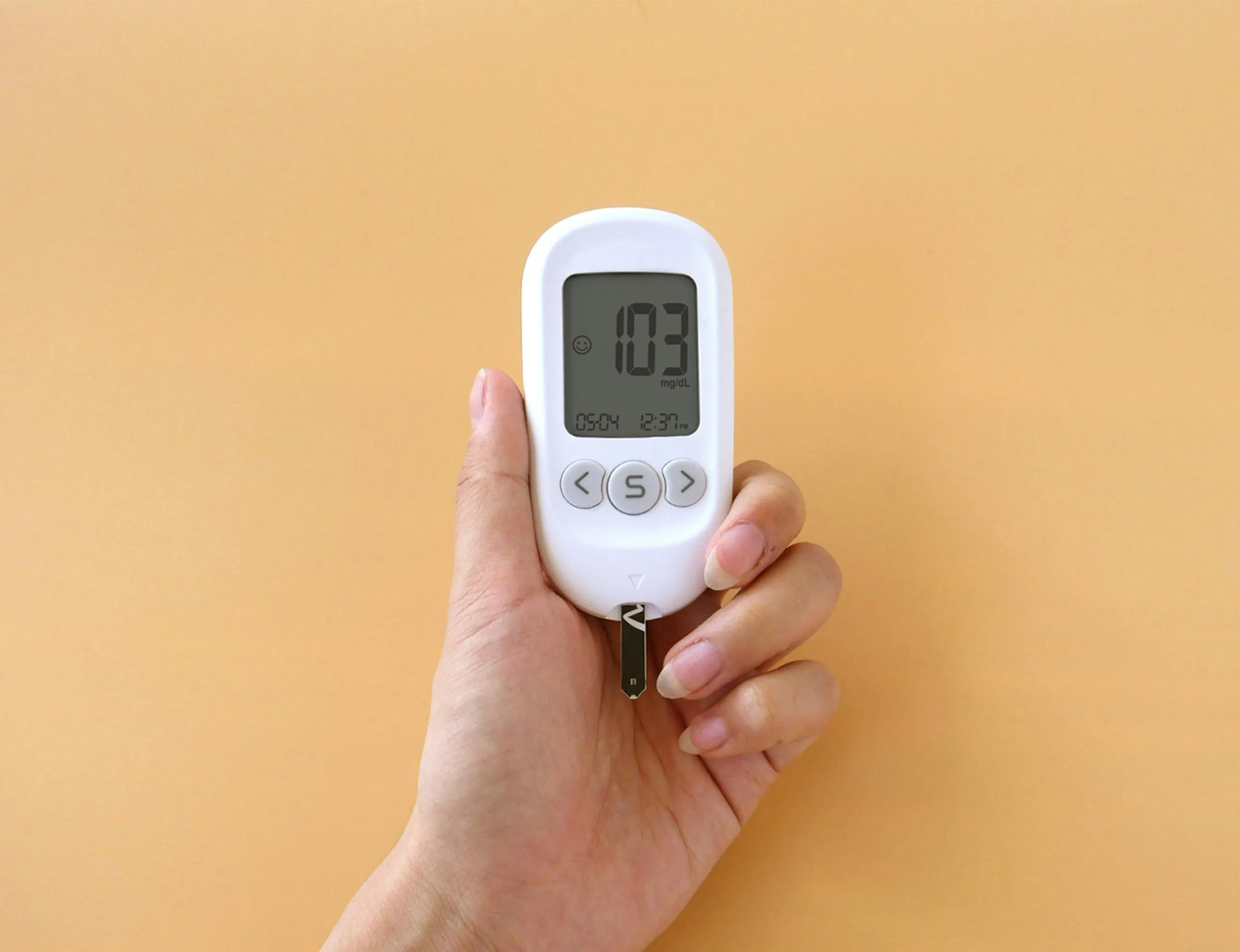 Hand holding a glucose meter showing a reading of 103 mg/dL related to GCSE Combined Science insulin function quiz.