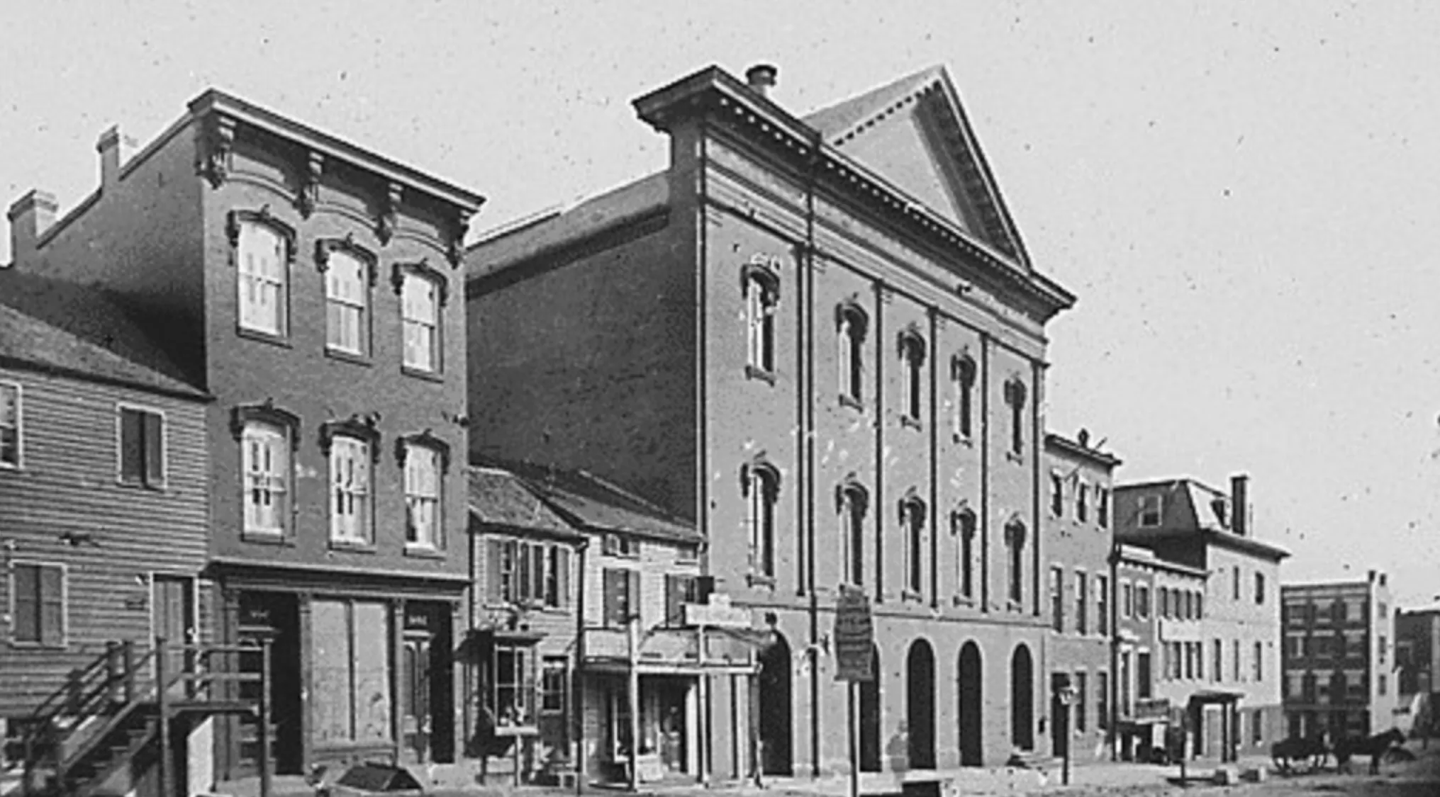 Historic black and white image of 19th century buildings on a street related to Abraham Lincoln assassination year.
