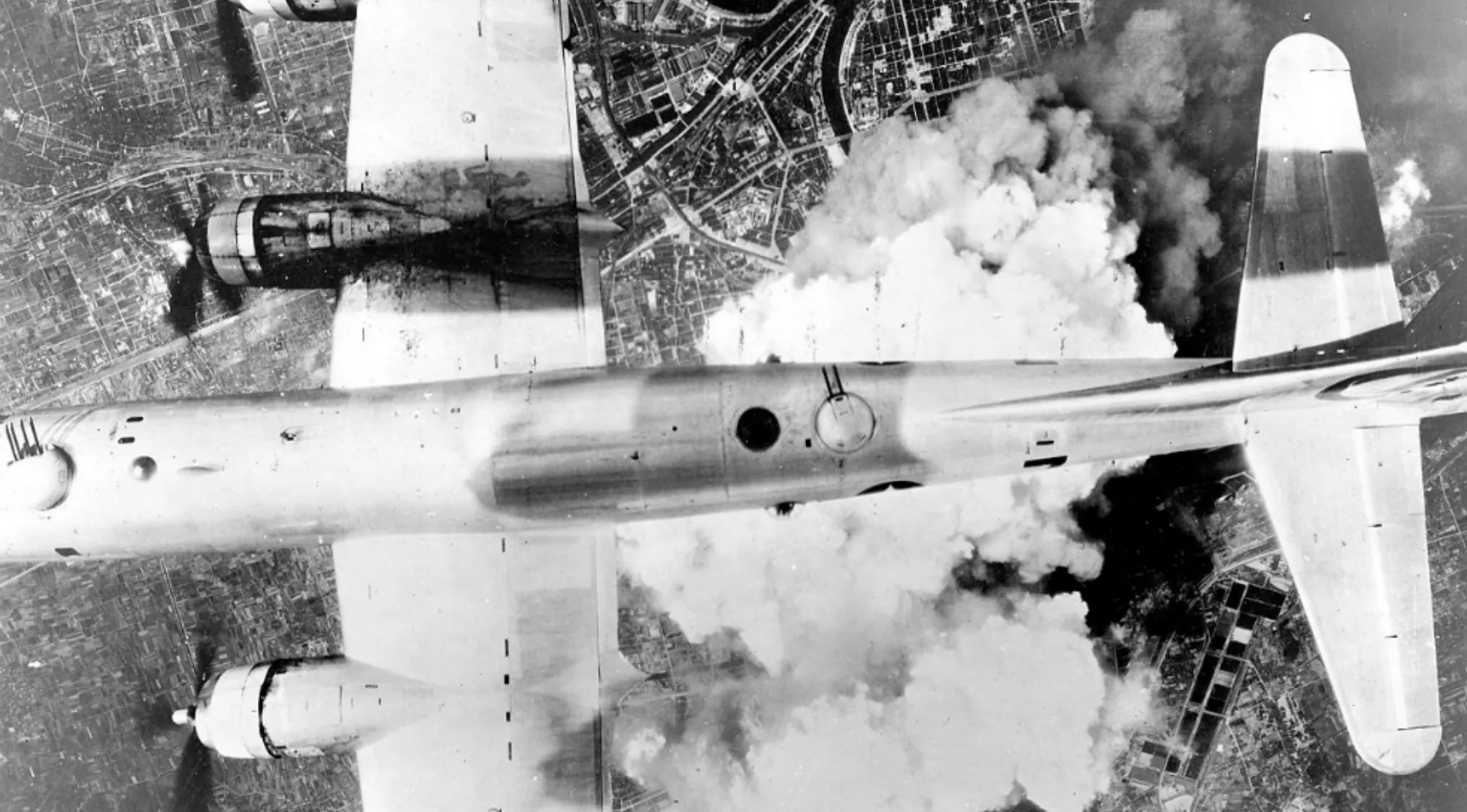B-29 bomber flying over Hiroshima during the atomic bombings in World War II, spreading massive smoke and destruction below.