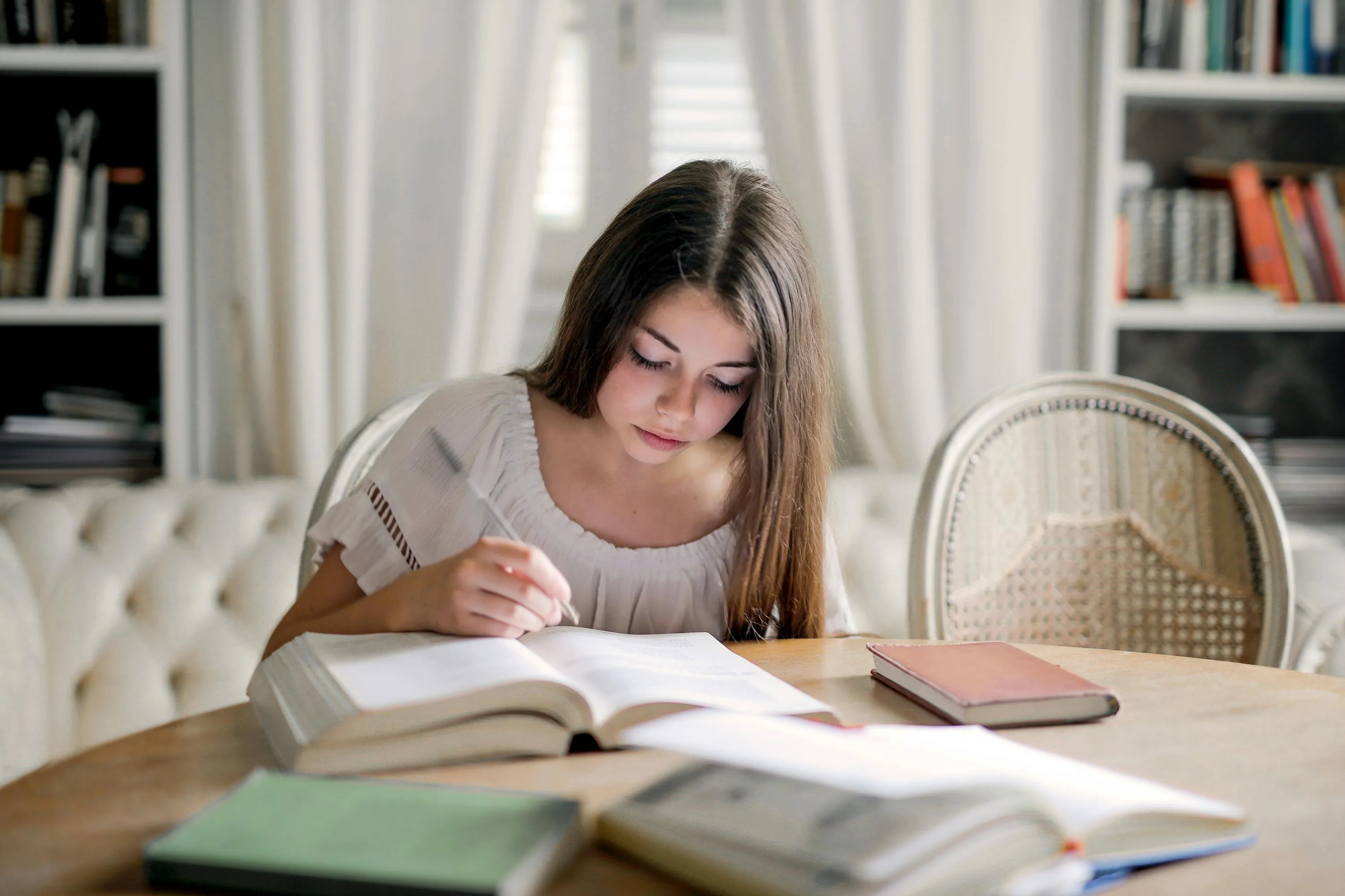 Young woman studying at a wooden table with books, focused on a difficult general knowledge quiz for high IQs.
