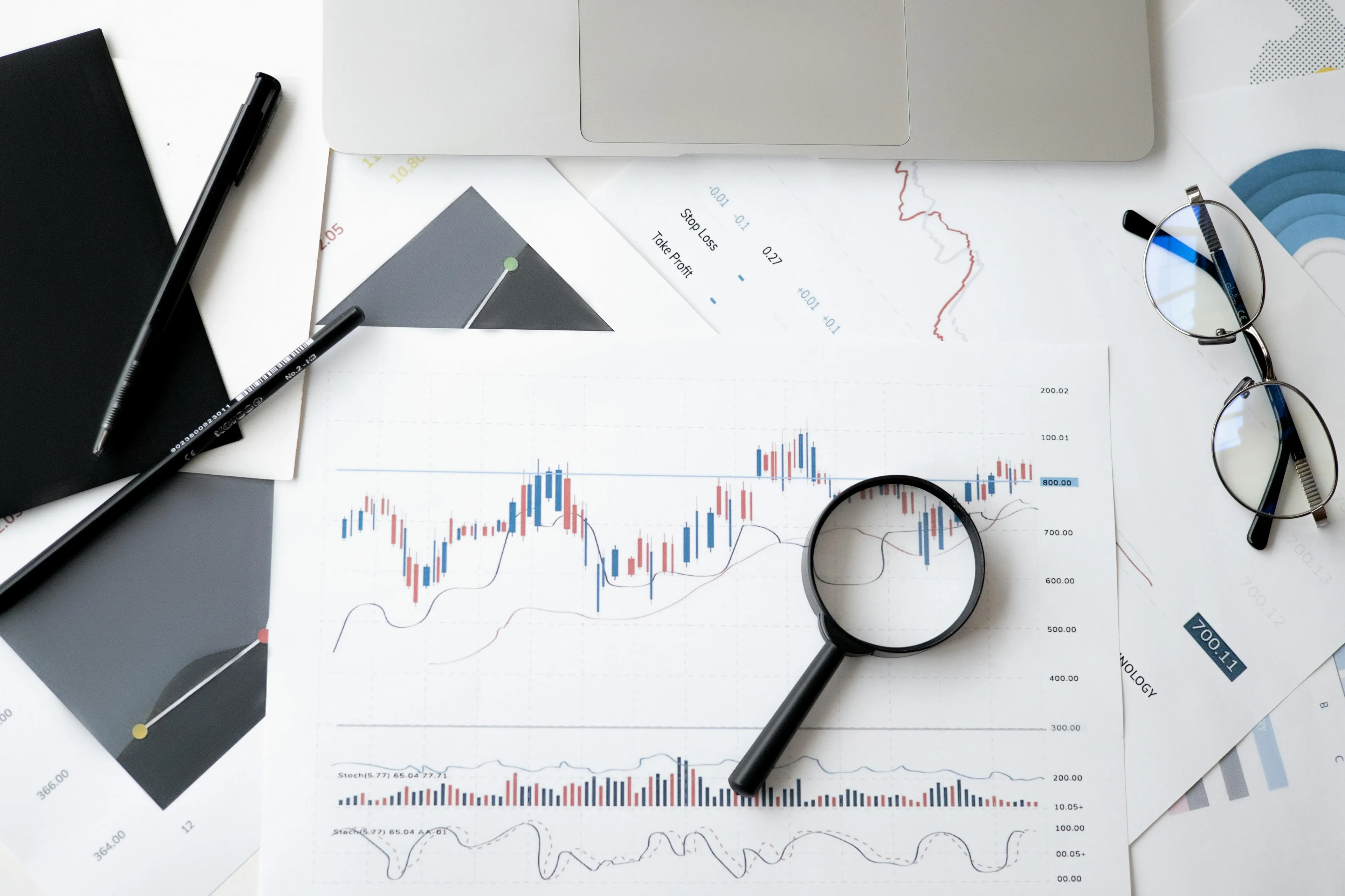 Magnifying glass on economic charts with laptop, glasses, and pens, symbolizing Keynesian economics analysis and quiz concept.