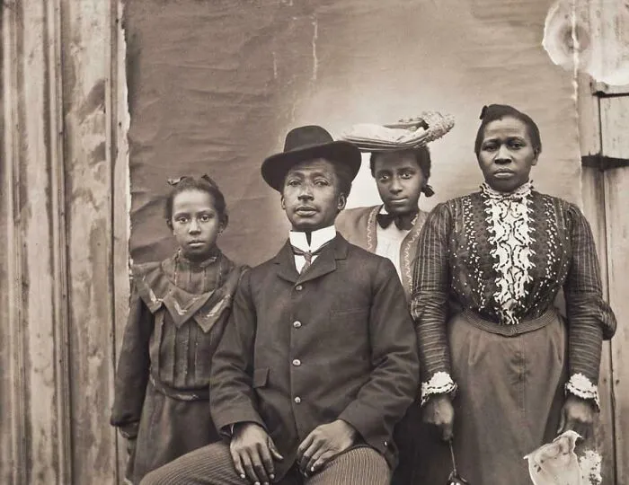 Black family in vintage historical garments posing for a formal portrait showcasing early 20th century fashion styles.