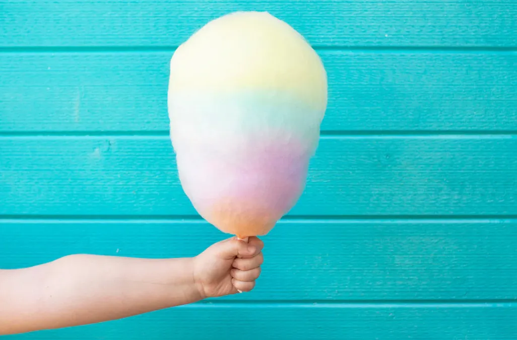Hand holding pastel-colored cotton candy against a turquoise wooden background for a movie snack choice.